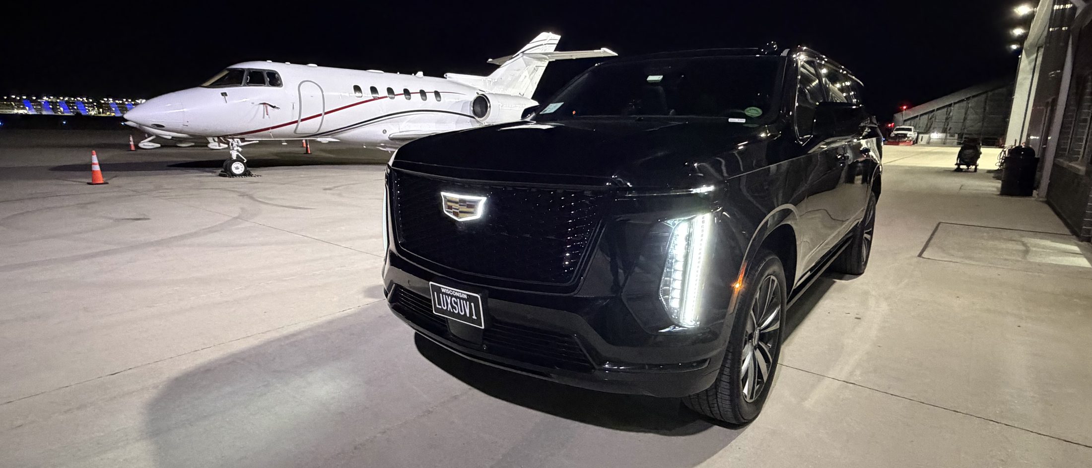 Black Cadillac Escalade ESV lit at night beside a private jet on the ramp at Jet Aviation, Milwaukee Mitchell